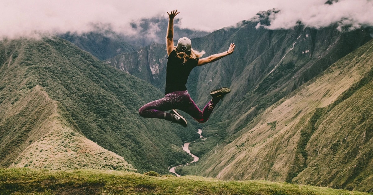 grateful woman jumping on top of mountain