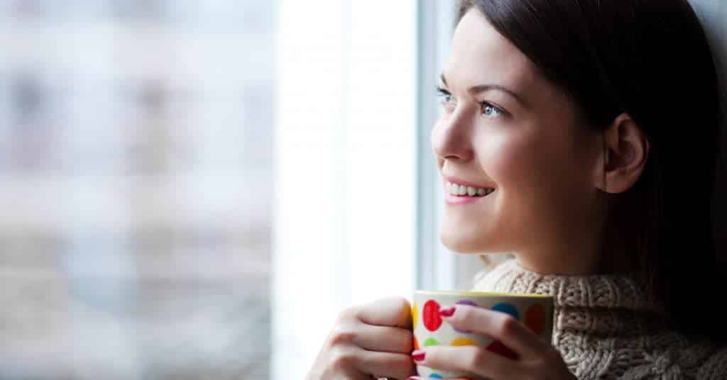 Woman drinking coffee reflecting on New Year's goals by a window