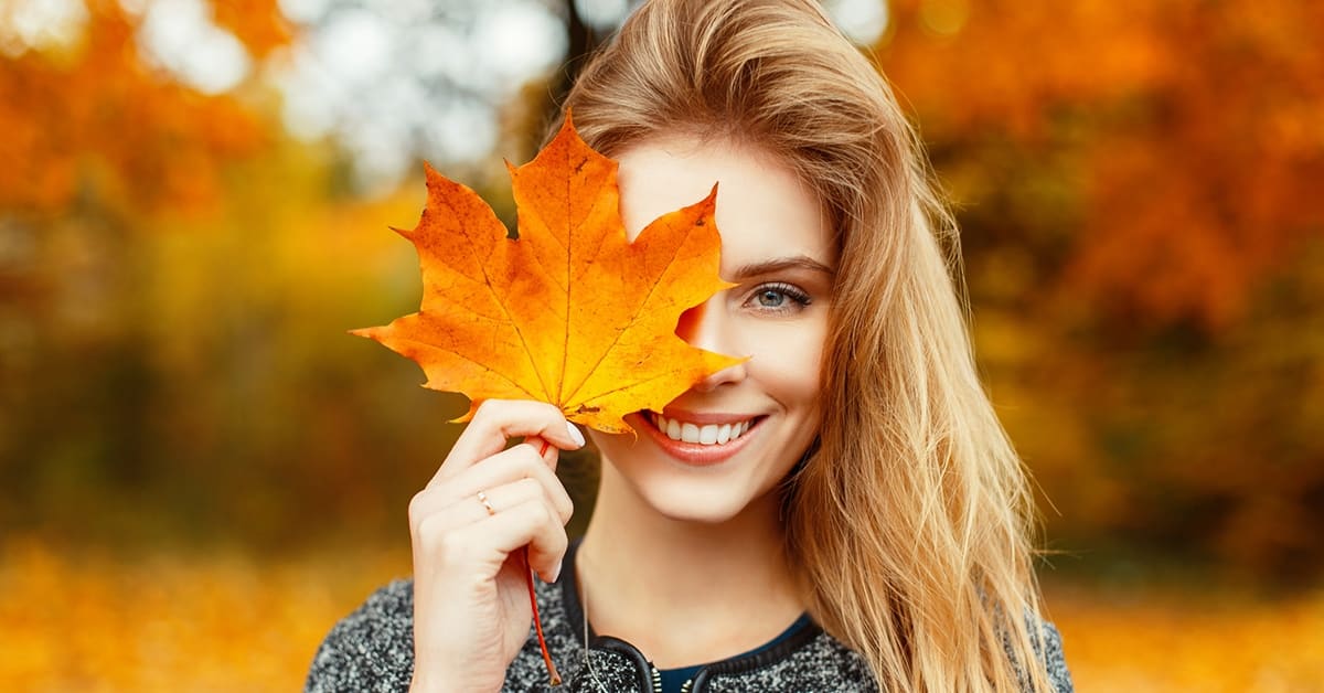 smiling woman holding large maple lead over eye in autumn